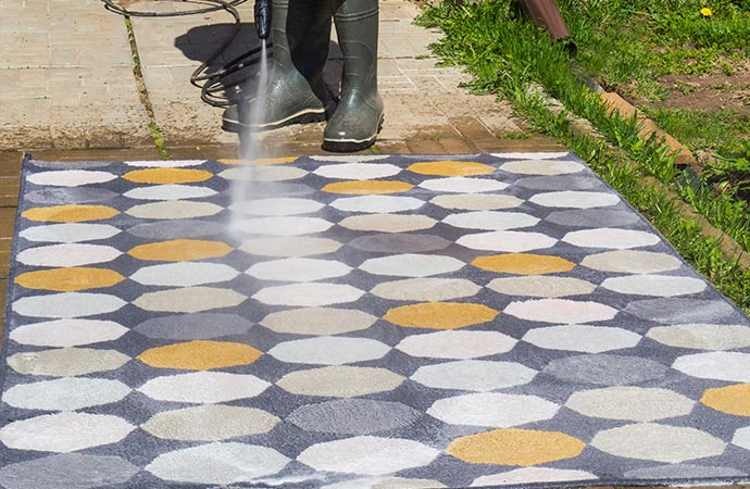 man washing rug with pressure washer outdoors